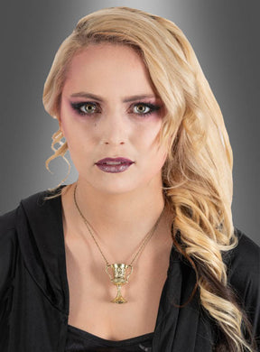 Eine Frau mit langen blonden Haaren, violettem Augen-Make-up und dunklem Lippenstift trägt ein schwarzes Oberteil und die „Goldene Kette mit Kelch-Anhänger“ – deren Kelch-Anhänger an die Magie von Harry Potter erinnert –, während sie vor einem grauen Hintergrund mit Farbverlauf posiert.