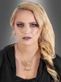 Eine Frau mit langen blonden Haaren, violettem Augen-Make-up und dunklem Lippenstift trägt ein schwarzes Oberteil und die „Goldene Kette mit Kelch-Anhänger“ – deren Kelch-Anhänger an die Magie von Harry Potter erinnert –, während sie vor einem grauen Hintergrund mit Farbverlauf posiert.
