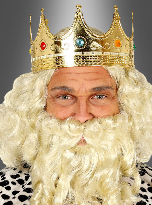 Eine Person, die eine Königskrone aus Gold mit Edelsteinen, eine lockige blonde Perücke und einen dazu passenden Bart trägt und eine schwarz-weiß gepunktete Robe trägt.