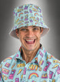 Ein lächelnder Mann trägt ein farblich passendes, farbenfrohes Shirt im 90er-Jahre-Stil und einen blauen Eimerhut mit 90er-Jahre-Motiv, der auf einem grauen Farbverlaufshintergrund mit Comicfiguren, Regenbögen und Kassetten verziert ist. Dieses lustige Retro-Party-Accessoire rundet seinen nostalgischen Look perfekt ab.