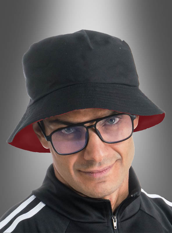 Ein Mann, der den „Wandelbarer 2-in-1-Eimerhut mit Brille“ – in Schwarz und Rot – sowie eine schwarze Jacke mit Reißverschluss und weißen Streifen trägt, verkörpert vor einem grauen Hintergrund mit Farbverlauf den klassischen 90er-Jahre-Look.