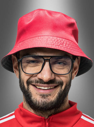 Ein Mann mit Bart und Brille trägt einen roten „Wandelbarer 2-in-1-Eimerhut mit Brille“ und eine dazu passende rote Jacke und lächelt vor einem grauen Hintergrund mit Farbverlauf – eine verspielte Anspielung auf den Karneval und den klassischen Outfit-Stil der 90er Jahre.