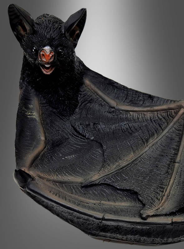 Eine Nahaufnahme der „Deluxe Fledermaus Schale 24 cm aus Kunstharz“ zeigt eine auffällige schwarze Fledermaus mit ausgebreiteten Flügeln und gefletschten Zähnen vor einem grauen Hintergrund mit Farbverlauf – perfekt, um Ihrer Halloween-Dekoration einen geheimnisvollen Touch zu verleihen oder als faszinierender Blickfang in Ihrer gotischen Tischdekoration.