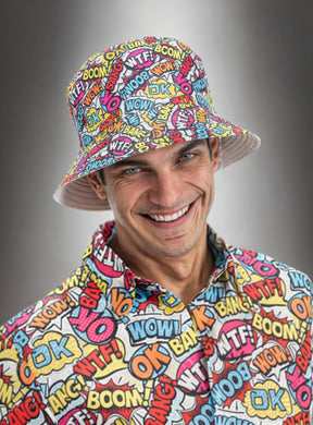 Ein lächelnder Mann, der einen Eimerhut im Comic-Stil und ein dazu passendes T-Shirt trägt, auf denen jeweils farbenfrohe Wörter im Comic-Stil wie „WOW!“, „BANG!“, „OK“ und „WTF?“ vor einem grauen Farbverlaufshintergrund zu sehen sind.