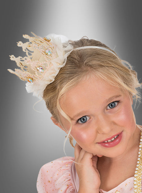 Ein junges Mädchen mit blonden Haaren trägt eine „Robuste Prinzessin“-Krone und ein mit Perlen verziertes rosa Kleid und posiert vor einem grauen Hintergrund mit Farbverlauf.