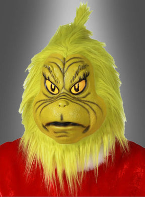 Eine Person, die die gelbe Original-Der-Grinch-Latexmaske und ein rotes Kostüm trägt, posiert vor einem grauen Hintergrund mit Farbverlauf.