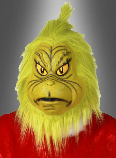 Eine Person, die die gelbe Original-Der-Grinch-Latexmaske und ein rotes Kostüm trägt, posiert vor einem grauen Hintergrund mit Farbverlauf.