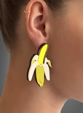 Nahaufnahme des Ohrs einer Person, die große, farbenfrohe Acryl-Ohrringe in Form einer Banane sowie einen kleinen goldenen Creolenring im oberen Ohrbereich trägt, was den verspielten Modeschmuck-Stil unterstreicht.