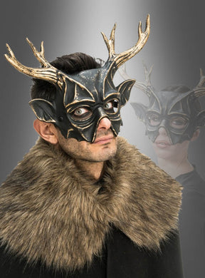 Eine Person, die die „Edle Maske 30 cm mit Hörnern, schwarz-gold“ und einen Umhang aus Kunstfell trägt, blickt in die Kamera, während im Hintergrund eine verblasste Kopie der maskierten Figur zu sehen ist.