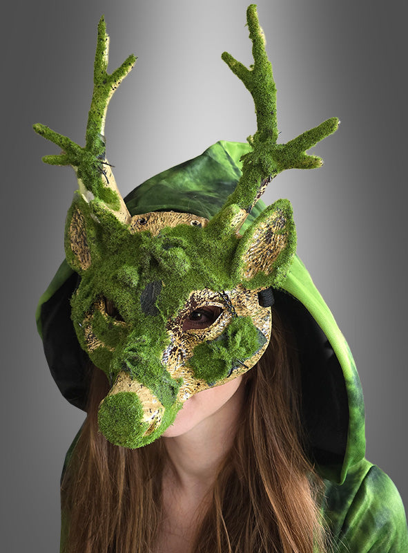 Eine Person, die eine grüne Kapuze und die mit Kunstmoos bedeckte „Moos Effekt Reh-Maske mit Geweih“ trägt, vor einem grauen Hintergrund mit Farbverlauf.