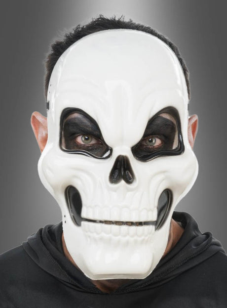 Eine Person, die die „Weiße Totenkopf-Halbmaske für Erwachsene“ und einen schwarzen Kapuzenpulli trägt, blickt vor einem schlichten grauen Hintergrund nach vorne.