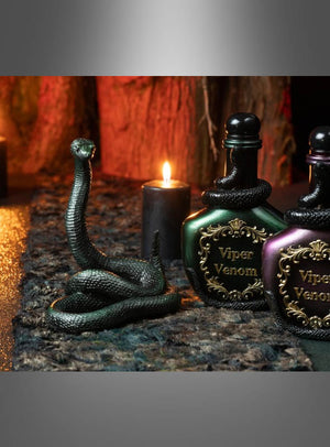 Eine realistisch gestaltete Schlangenfigur steht neben zwei dekorativen Flaschen mit der Aufschrift „Viper Venom“ auf einem Tischläufer aus Kunstfell (300 cm, Moos-Effekt), im Hintergrund brennen Kerzen – so entsteht eine auffällige Dekoration für eine Fantasy-Party, die Ihrem Ambiente einen mystischen Charme verleiht.