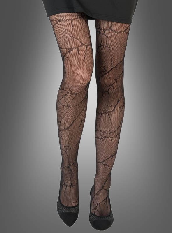 Eine Person, die eine schwarze gemusterte Strumpfhose – genauer gesagt die „Strumpfhose Dornen Ranken Muster“ – und einen schwarzen Rock trägt und vor einem grauen Hintergrund steht. Zu sehen sind nur der Unterkörper und die Füße in schwarzen Schuhen.