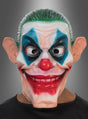Eine Person, die die „Horror Clown Joker“-Vollmaske trägt – mit übertrieben großen Ohren, grünen Haaren, blauem Augen-Make-up, einer roten Nase und einem breiten, aufgemalten Grinsen –, steht vor einem grauen Hintergrund.
