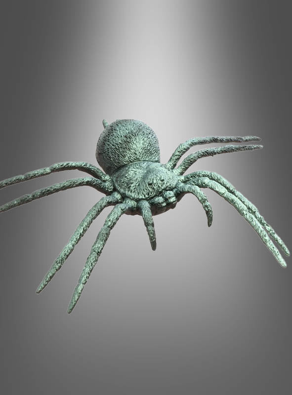 Eine realistisch gestaltete Metallspinnen-Skulptur mit dem Titel „Spinne Halloween 23 cm grün irisierend“, die acht Beine und schimmernde, grün-irisierende Akzente am Körper aufweist, wird vor einem neutralen grauen Hintergrund mit einem Spotlicht-Effekt mit Farbverlauf präsentiert – was sie zu einer auffälligen Halloween-Dekospinne macht.