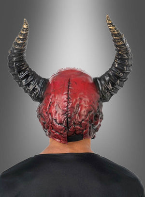 Eine Person, die die auffällige „Roter Dämon mit Hörner Maske Deluxe“ trägt – eine rot-schwarze Vollgesichtsmaske mit Hörnern –, ist von hinten vor einem grauen Hintergrund mit Farbverlauf zu sehen.