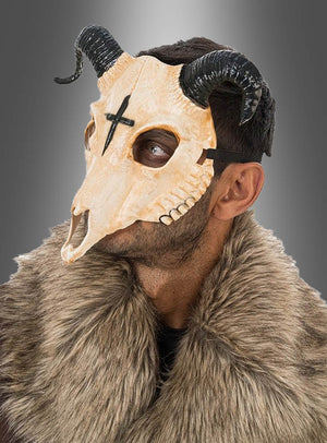Ein Mann, der eine „Gehörnte Tierschädel-Halbmaske“ mit schwarzen Hörnern und einem Pelzkragen trägt und zur Seite blickt. Auf der Stirn der Maske ist ein markantes schwarzes Kreuz zu sehen.