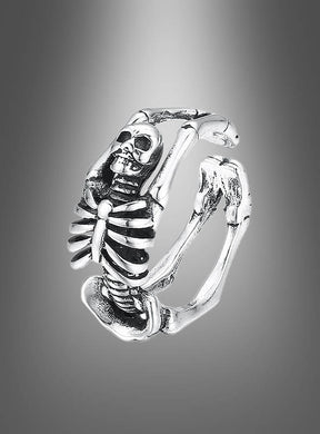 Ein verstellbarer Skelettring als Halloween-Schmuck aus Silber, kunstvoll gestaltet mit detailliertem Rippengeflecht, Schädel und Armknochen, präsentiert vor einem sanft verlaufenden grauen Hintergrund.