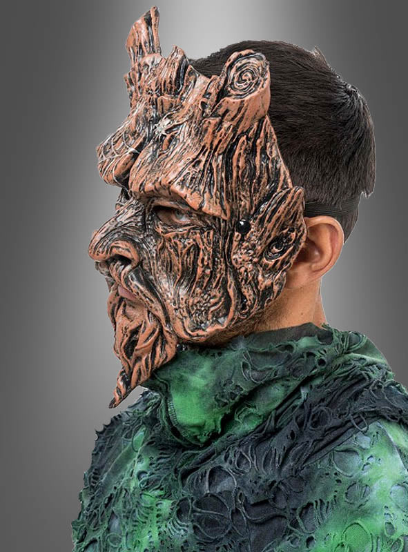 Eine Person im Profil trägt eine detailreiche „Waldgeist Baum“-Halbmaske und ein strukturiertes grünes Kostüm, das an Laub erinnert, vor einem einfarbigen Hintergrund mit Farbverlauf.