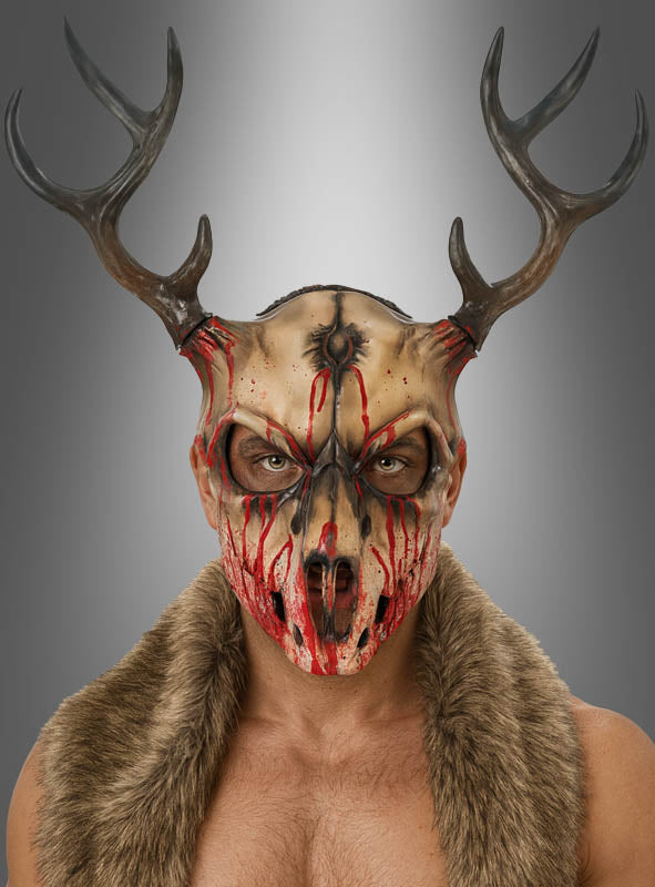 Eine Person, die die „Blutiger Hirsch Skelett-Maske“ trägt – entworfen im Stil einer Schaumstoff-Tierschädelmaske mit markantem Geweih und realistisch wirkendem Kunstblut –, steht in einer Pelzweste vor einem neutralen Hintergrund und blickt nach vorne. Diese unverwechselbare Halloween-Verkleidung strahlt eine unheimliche, unvergessliche Präsenz aus.