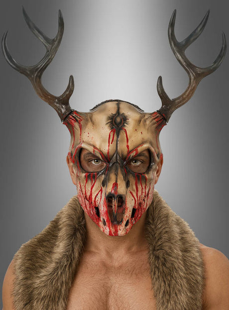 Eine Person, die die „Blutiger Hirsch Skelett-Maske“ trägt – entworfen im Stil einer Schaumstoff-Tierschädelmaske mit markantem Geweih und realistisch wirkendem Kunstblut –, steht in einer Pelzweste vor einem neutralen Hintergrund und blickt nach vorne. Diese unverwechselbare Halloween-Verkleidung strahlt eine unheimliche, unvergessliche Präsenz aus.