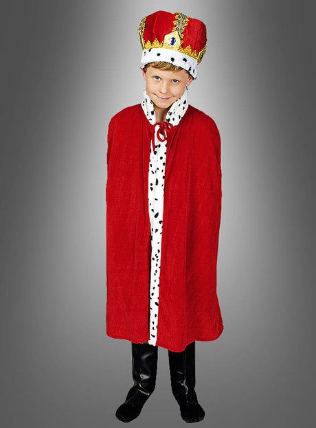 Ein Kind, das einen roten Königsmantel für Kinder mit einem Kragen aus Kunsthermelin, eine mit Edelsteinen besetzte Krone und schwarze Stiefel trägt, steht vor einem schlichten grauen Hintergrund.