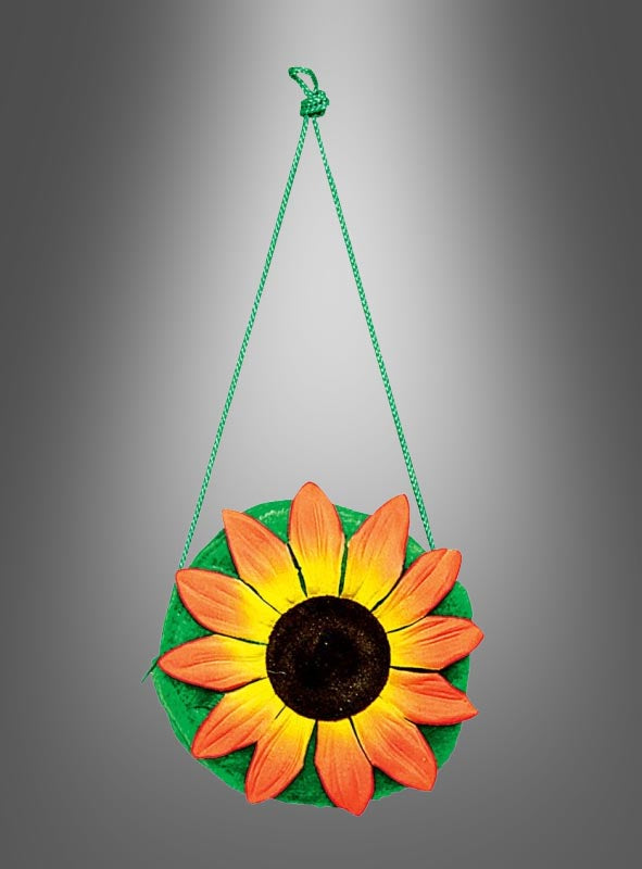 Ein rundes, grünes Ornament mit einem orange-gelben Sonnenblumenmotiv, inspiriert von der „Sonnenblumen-Handtasche“, hängt an einer grünen Schnur vor einem grauen Hintergrund mit Farbverlauf.