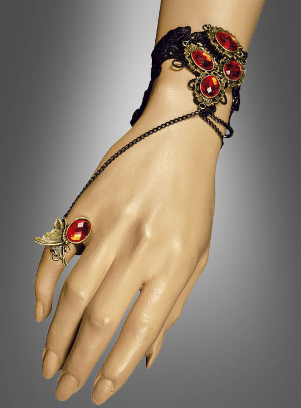 Eine Hand, geschmückt mit dem „Handschmuck mit roten Schmucksteinen“ – einem Armband im Vintage-Stil mit roten Edelsteinen, schwarzer Spitze und einem Ring, der durch zarte Ketten mit einem roten Edelstein und einem Schmetterlingsdetail verbunden ist – macht sie zu einem idealen Accessoire für ein Vampir-Kostüm.