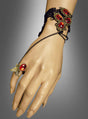 Eine Hand, geschmückt mit dem „Handschmuck mit roten Schmucksteinen“ – einem Armband im Vintage-Stil mit roten Edelsteinen, schwarzer Spitze und einem Ring, der durch zarte Ketten mit einem roten Edelstein und einem Schmetterlingsdetail verbunden ist – macht sie zu einem idealen Accessoire für ein Vampir-Kostüm.