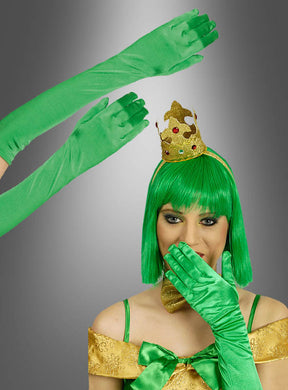 Eine Person mit grüner Perücke, goldener Krone und goldenem Kleid, die extra lange grüne Satinhandschuhe (47 cm) trägt, hält sich die Hand vor den Mund; zwei Hände in denselben grünen Handschuhen ragen vor diesem grauen Hintergrund empor.