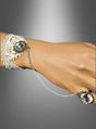 Eine Hand, geschmückt mit dem Steampunk-Handschmuck-Set mit Spitze, bestehend aus einem auffälligen Edelsteinarmband, das über eine zarte Kette mit einem passenden Edelsteinring verbunden ist, präsentiert vor einem grauen Hintergrund mit Farbverlauf – ein exquisites Accessoire, das jedes Steampunk-Outfit aufwertet oder Ihren Look abrundet.