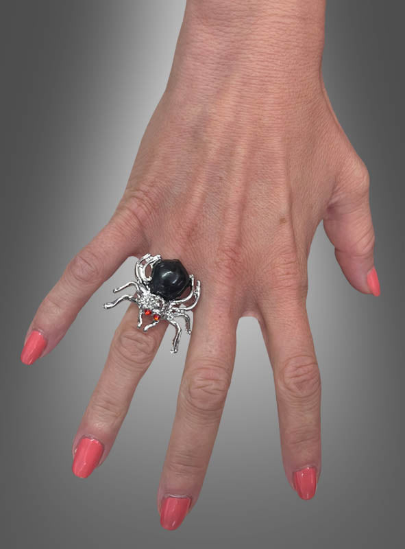 Eine Hand mit korallenfarbenen Nägeln trägt den „Verstellbaren Ring mit Spinne“ – einen auffälligen, spinnenförmigen Silberring mit einem markanten schwarzen Stein – am Mittelfinger. Damit eignet er sich perfekt als Halloween-Schmuck oder für alle, die auffällige Accessoires lieben.