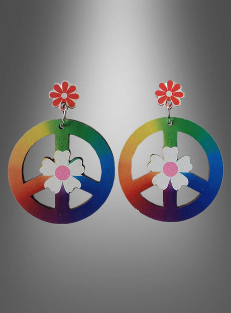 Ein Paar Ohrringe mit Regenbogen-Friedenszeichen und weißen Blumen, die jeweils an einem rot-weißen, gänseblümchenförmigen Ohrstecker hängen, präsentiert vor einem grauen Hintergrund mit Farbverlauf – diese „Peace Zeichen“-Ohrringe für Hippies aus Holz sind das perfekte Hippie-Schmuckstück für jeden Freigeist.