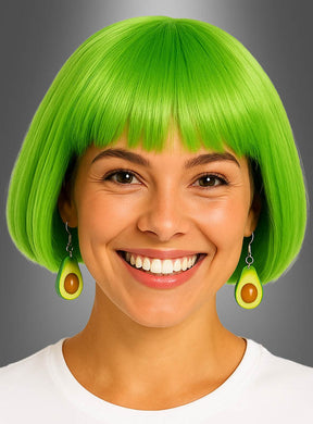 Eine lächelnde Person mit einem leuchtend grünen Bob-Haarschnitt, die Avocado-Ohrringe als Kostümschmuck und ein weißes Hemd trägt, vor einem grauen Hintergrund mit Farbverlauf.