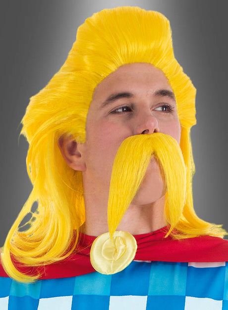 Eine Person, die die leuchtend gelbe Perücke und den Schnurrbart aus dem „Troubadix Perücke und Bart“-Lizenzprodukt des Asterix-Sets trägt, kombiniert mit einem blau karierten Outfit und einem roten Umhang mit einem runden gelben Medaillon, steht vor einem grauen Hintergrund und sorgt so für einen authentischen Look im Stil eines gallischen Barden.
