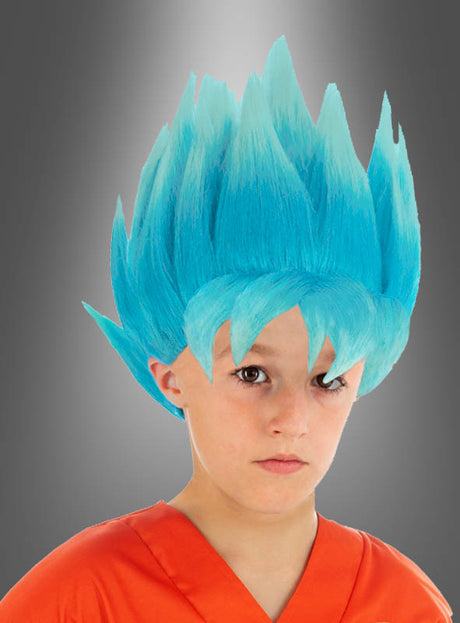 Ein Kind trägt die „Son-Goku-Kinderperücke blau aus Dragon Ball Super“ sowie ein orangefarbenes T-Shirt und posiert mit ausdruckslosem Gesicht vor einem grauen Hintergrund mit Farbverlauf; die blaue, stachelige Perücke erinnert an Son Gokus Verwandlung in den Super-Saiyajin Blue.