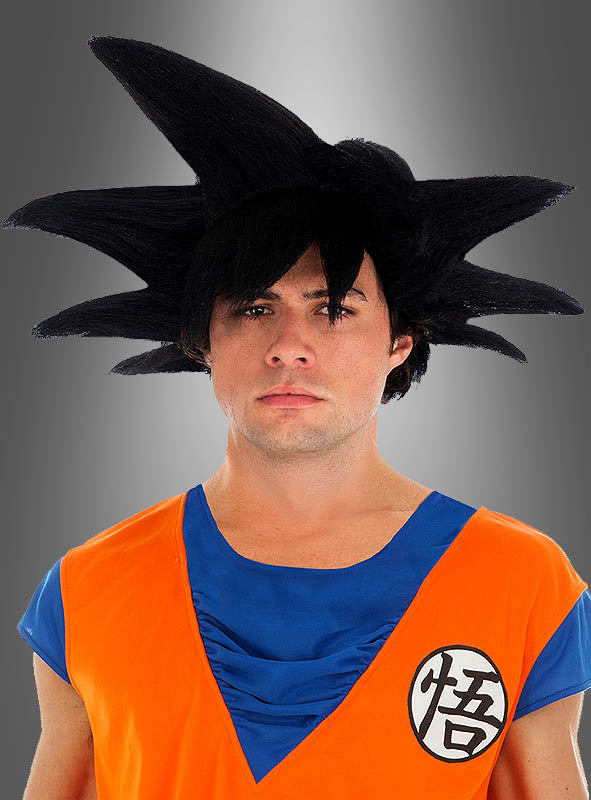Eine Person, die ein orange-blaues Saiyajin-Kostüm mit einer stacheligen schwarzen Son-Goku-Perücke für Erwachsene aus „Dragonball“ trägt und einer Anime-Figur ähnelt, steht vor einem grauen Hintergrund mit Farbverlauf.