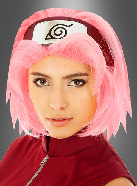 Eine Person, die eine rosa „Sakura“-Perücke für Erwachsene, ein rotes Outfit und ein Stirnband mit einem stilisierten Wirbel-Symbol trägt, posiert vor einem grauen Hintergrund mit Farbverlauf für ein beeindruckendes „Naruto Shippuden“-Cosplay.