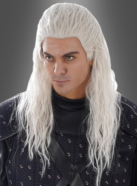Eine Person mit langen, welligen weißen Haaren – die an die „Witcher Langhaar-Perücke weiß“ erinnern – in einem schwarzen, mittelalterlich anmutenden Outfit steht vor einem schlichten grauen Hintergrund.