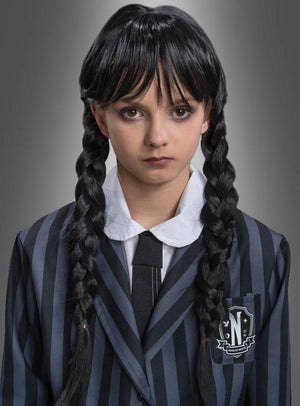 Eine Person, die die „Wednesday“-Perücke für Kinder mit langen, schwarzen Zöpfen trägt, kombiniert diese vor einem neutralen Hintergrund perfekt mit einem schwarz-grau gestreiften Blazer, einem weißen Hemd und einer schwarzen Krawatte – eine tolle Wahl für ein „Addams Family“-Kostüm.