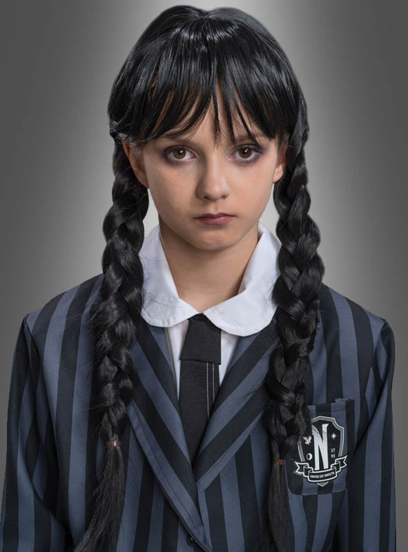 Eine Person, die die „Wednesday“-Perücke für Kinder mit langen, schwarzen Zöpfen trägt, kombiniert diese vor einem neutralen Hintergrund perfekt mit einem schwarz-grau gestreiften Blazer, einem weißen Hemd und einer schwarzen Krawatte – eine tolle Wahl für ein „Addams Family“-Kostüm.