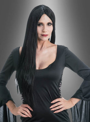 Eine Frau mit langen schwarzen Haaren und einem schwarzen Kleid steht mit den Händen in den Hüften vor einem neutralen Farbverlaufshintergrund und verkörpert damit perfekt den Stil der Original-Morticia-Perücke aus „Wednesday“ – ideal für Halloween-Cosplay oder jeden von der Addams-Familie inspirierten Look.