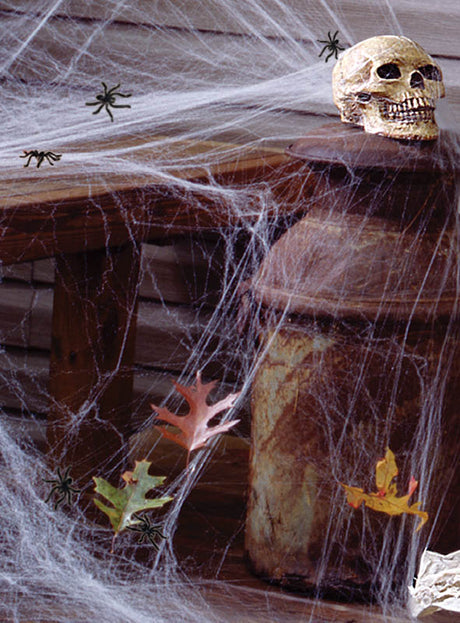 Ein Plastikschädel ruht auf einem rostigen Kanister, der mit „Leuchtendes Spinnennetz Halloween 60 g“-Spinnennetzen drapiert ist, dazwischen liegen Spielzeugspinnen und Papierblätter verstreut – eine ideale Ergänzung für Ihre Halloween-Dekoration.