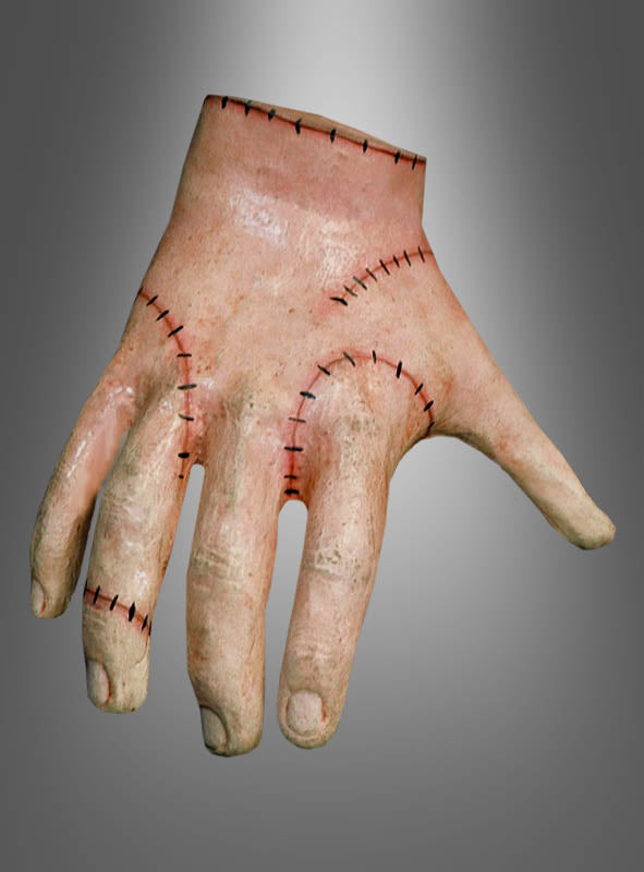 Eine abgetrennte Hand mit sichtbaren Nähten am Handgelenk und über die Finger hinweg, die den Eindruck eines zusammengesetzten Ganzen erweckt; gestaltet in Anlehnung an den „Eiskaltes Händchen“-Schulterhocker aus „Wednesday“, vor einem glatten grauen Hintergrund mit Farbverlauf.