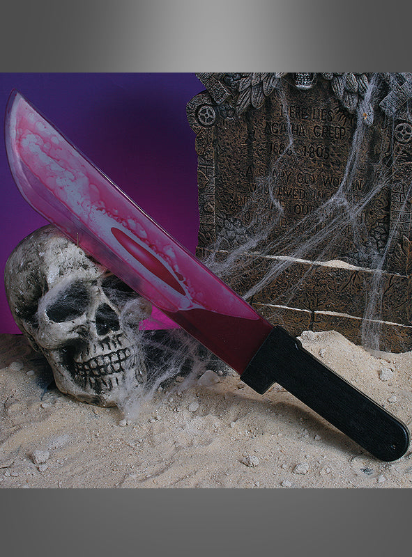 Eine „SCREAM“ blutige Machete (54 cm) aus Kunststoff ruht auf einem Schädel, umgeben von Spinnweben, Sand und einem Grabstein im Hintergrund.
