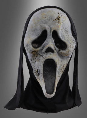 Die Original-„Scream“-Zombie-Maske mit einem weißen, rissigen Gesicht, einem langen, offenen Mund und hohlen Augen, die mit schwarzem Stoff drapiert ist, wird vor einem grauen Hintergrund mit Farbverlauf präsentiert.