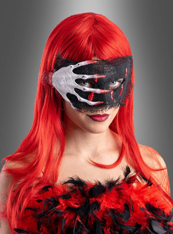 Eine Person mit langen roten Haaren und einem roten, mit Federn verzierten Outfit trägt die Halloween-Augenmaske – eine einzigartige Maske, die so gestaltet ist, dass sie einer Hand ähnelt, die die Augen bedeckt – vor einem grauen Hintergrund mit Farbverlauf.