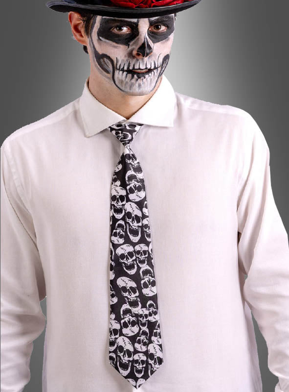 Eine Person, die ein weißes Hemd, eine Totenkopf-Krawatte für Halloween und einen Hut trägt und deren Gesicht mit einem schwarz-weißen Totenkopf-Motiv bemalt ist.