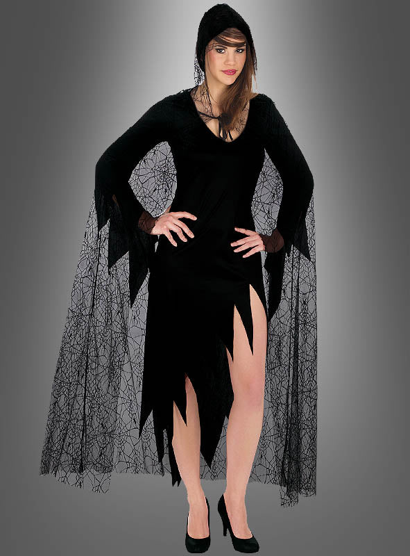 Vor einem grauen Hintergrund steht eine Frau mit den Händen in die Hüften gestemmt. Sie trägt ein schwarzes Kleid mit gezackten Säumen, lange Netzärmel mit einem Spinnennetz-Muster, schwarze High Heels und den Spinnennetz-Umhang für Hexen und Vampire – einen Umhang mit Kapuze, der an einen Halloween-Look erinnert.