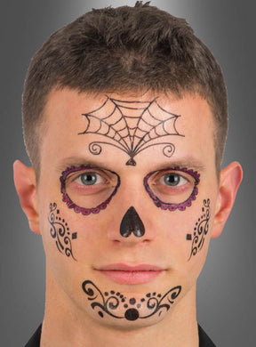 Ein Mann mit kurzen braunen Haaren trägt schwarze und violette „Sugar Skull“-Gesichtsbemalung – mit einem Spinnennetz-Motiv auf der Stirn, verzierten Augenringen, einer schwarzen Nase sowie kunstvollen Details auf den Wangen und am Mund –, die dem „Tattoo Day of the Dead“-Gesichtstattoo ähnelt.